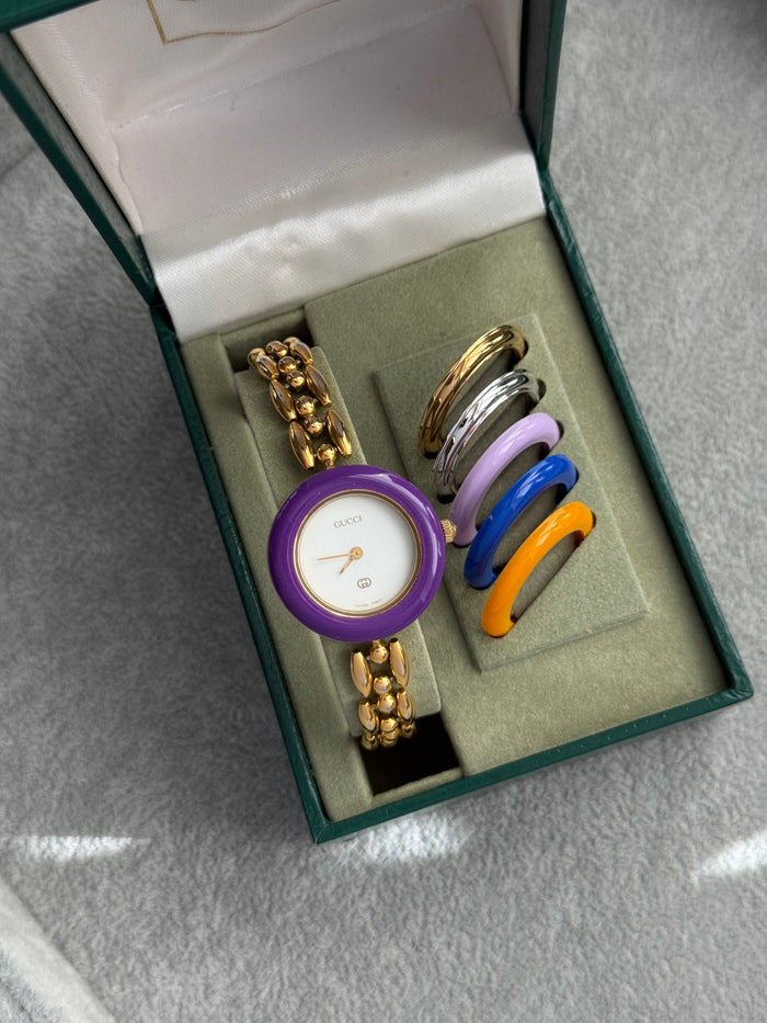 Vintage Gucci bezel watch with purple bezel and five spare bezels beside it in the original box